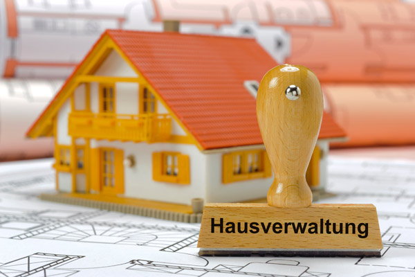 Ein kleines Modellhaus mit einem Stempel, auf dem Hausverwaltung steht, vor Bauplänen.